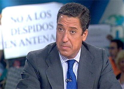 Eduardo Zaplana, ayer, en el programa <i>La Respuesta</i> mientras los trabajadores de Antena 3 muestran sus pancartas de protesta.