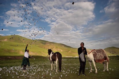 Un jinete nómada tibetano lanza, tan alto como puede, hojas de papel con plegarias escritas que darán buena suerte para la siguiente carrera, en la meseta tibetana, en el condado de Yushú (China).