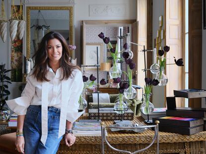 Cordelia de Castellane, directora creativa de Dior Maison y Baby Dior, posa en uno de los salones de su casa. La diseñadora lleva camisa blanca y vaqueros de Dior. El escritorio de ratán lo rescató de su casa de campo en L’Oise. Sobre él, unos antiguos matraces volumétricos de laboratorio que funcionan como jarrones.