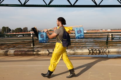 Un voluntario carga con una escoba y agua mientras cruza la pasarela peatonal que conecta Valencia con su pedanía de La Torre.