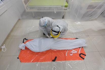 Dos sanitarios preparan el cuerpo de un paciente que sucumbió al coronavirus, en una sala de aislamiento en el hospital general de Bogor, Java Occidental (Indonesia).