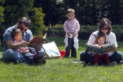 Una pareja con sus niños pequeños sentados en el césped del Retiro, hojeando cuentos durante la Feria del Libro.