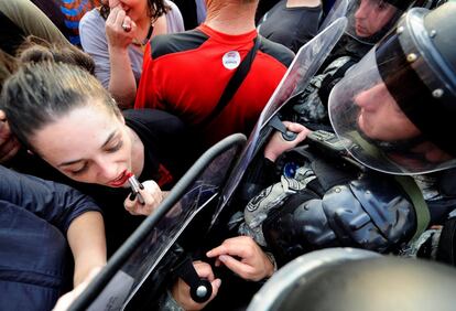 Una mujer se pinta los labios frente al escudo de un policía junto al edificio del gobierno macedonio en Skopje (Macedonia).