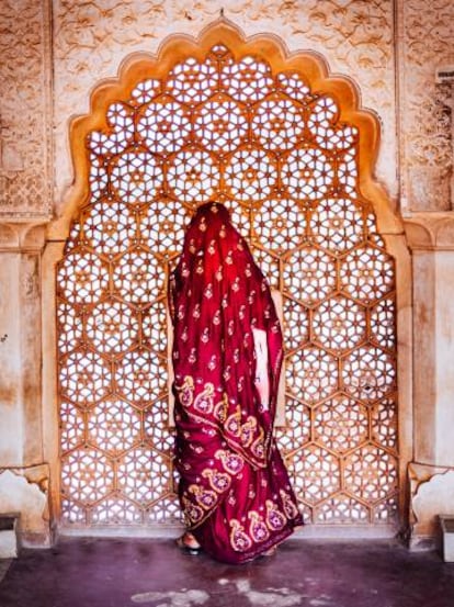 Una mujer vestida con un sari, frente a una ventana con calados de piedra en el fuerte de Amber de Jaipur (India).