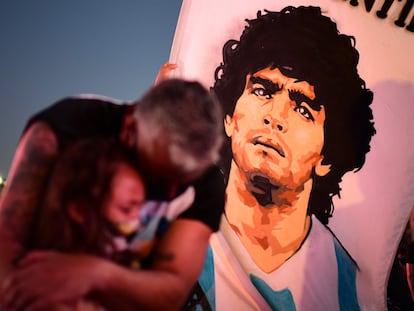 Dos personas lloran la muerte de Maradona junto a una bandera del futbolista, en Buenos Aires.