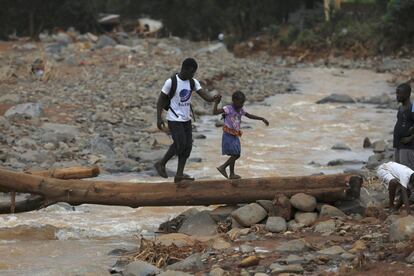 Un hombre ayuda a una niña a cruzar un puente con un tronco después de que las inundaciones se hayan llevado por delante el puente de cemento cerca de Freetown, la capital de Sierra Leona. 