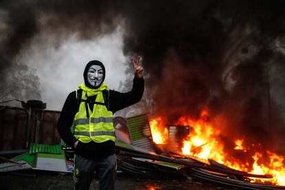 Un manifestante que usa una máscara de 'Guy Fawkes' hace el signo de la victoria cerca de una barricada en llamas, durante una protesta de los chalecos amarillos en París (Francia).