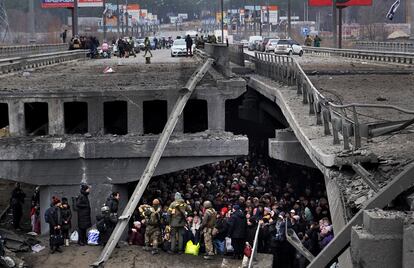 Ucranios intentan pasar por debajo de un puente destruido en Irpin, cerca de Kiev.