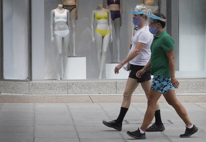 Dos transeúntes con pantallas de protección pasan frente a una tienda en Oxford Street, Londres (Reino Unido).