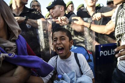 Un ni&ntilde;o llora mientras un grupo de refugiados sirios camina entre polic&iacute;as antidisturbios por una carretera en Edirne, en la frontera de Turqu&iacute;a con Grecia.