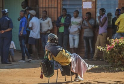 Una mujer sentada frente a una cola de votantes en Harare (Zimbabue).