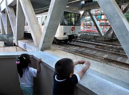 Dos niños desde el balcón de su vivienda de Sants, Barcelona, observan pasar el metro por la estructura del cajón del AVE.