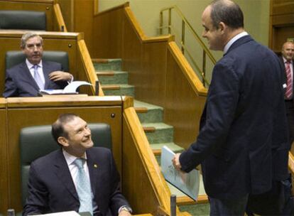 Joseba Egibar (de pie) se dirige a Ibarretxe, ambos sonrientes, durante la sesión del pleno del Parlamento vasco, ayer en Vitoria.