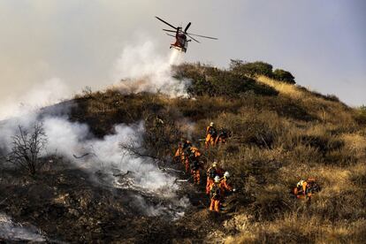 Bomberos extinguen un incendio forestal mientras un helicóptero del Departamento de Bomberos de Los Ángeles (LAFD) arroja líquido entre Glendale y Eagle Rock en Los Ángeles, California (EE UU). El incendio forzó el cierre de las autopistas 2 y 134 y las evacuaciones de los habitantes de la zona. 