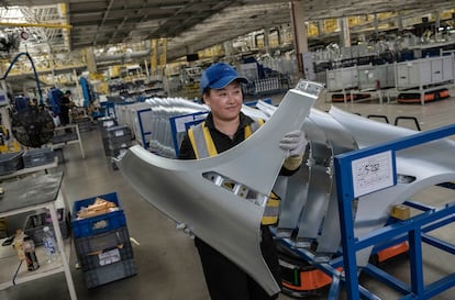 Una trabajadora lleva una pieza de automóvil mientras trabaja en la línea de producción del fabricante de vehículos eléctricos Zeekr el 29 de mayo en Ningbo (China)