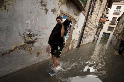 Un joven camina con su perro en brazos por una calle inundada en Tudela, Navarra.