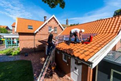 Dos obreros instalan paneles solares en el tejado de una casa.