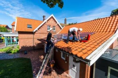 Dos obreros instalan paneles solares en el tejado de una casa.