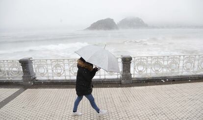 Una mujer se protege con una paraguas en la playa de Ondarreta.