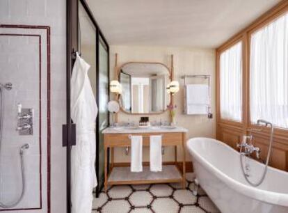 El baño de una de las habitaciones 'premiun', con cortinillas que recuerdan a las de la casa de la abuela, el suelo de azulejos de cerámica pequeños con dibujos geométricos, con tocador estilo 'mid-century' castellanizado y los azulejos de las paredes, con una encantadora imperfección y un dibujo en cenefa muy barrio de Salamanca.