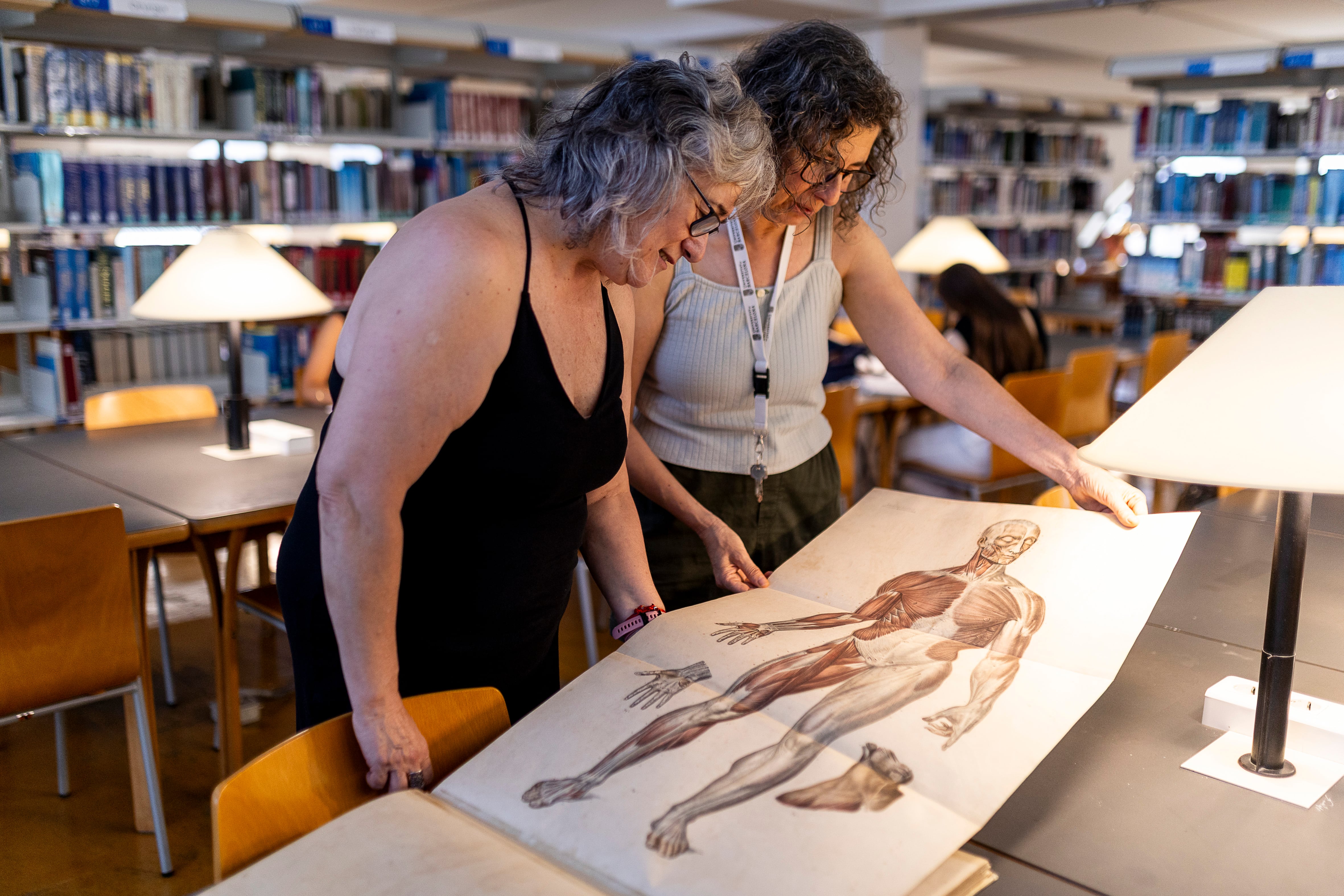 Rosa Zaborras (izq.) y Marta Mercader, bibliotecarias en la Facultad de Medicina de la Universidad de Barcelona consultan el libro 'Anatomie élémentaire', publicado el año 1843, donde predominan modelos masculinos para ilustrar el cuerpo humano.