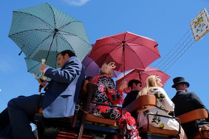 Varias personas montadas en un coche de caballos de la Feria de Abril de Sevilla se protegen del calor con sombrillas, este miércoles.
