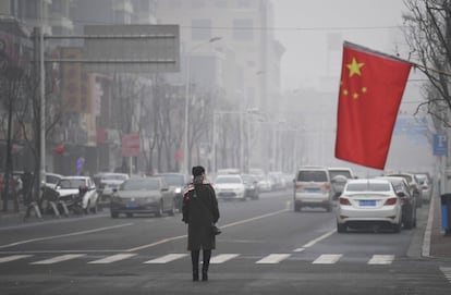 Una mujer cruza una calle cerca de una bandera nacional china entre la polución en Shijiazhuang (China), el 21 de diciembre de 2016.
