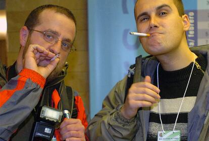 Dos fotógrafos posan ante las cámaras con sus pitillos recién encendidos en el primer día de trabajo en el que la prohibición de fuma se ha llevado a efecto en las empresas. Sanidad calcula que la ley hará que el 10% de los fumadores abandonen el hábito durante este año.