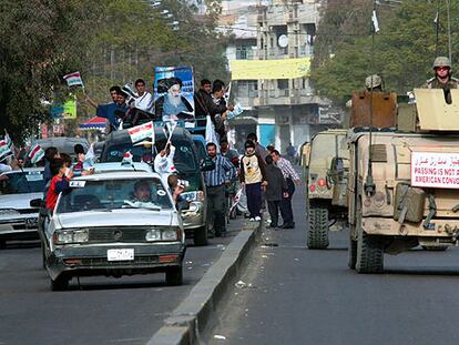 Una caravana electoral de partidarios del gran ayatolá Ali al Sistani pasa junto a un convoy militar de EE UU en Bagdad.