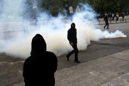 Dos manifestantes caminan en medio de gases lacrimógenos durante los enfrentamientos con la policia antidisturbios, en Atenas.