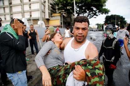 Un hombre lleva a una manifestante afectada por los gases lacrimógenos lanzados por la policía en el barrio Caria de Caracas.