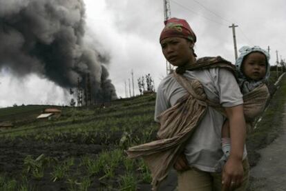 Una aldeana carga a su hijo mientras el volcán en erupción expulsa nubes de humo y cenizas.