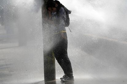 Una joven se protege del agua lanzada por la policía contra los manifestantes en Santiago.