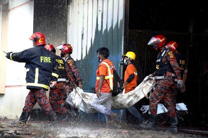 Varios bomberos trasladan el cuerpo sin vida de una de las víctimas de un incendio en una fábrica de alimentos cerca de Dacca, Bangladés. Al menos 52 personas murieron y otras 25 resultaron heridas en el incendio que comenzó en la fábrica de Alimentos y Bebidas de Hashem el jueves por la tarde y que los bomberos tardaron horas en sofocar.