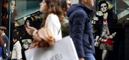 Varias personas pasan con bolsas de compras ante una de las tiendas de la c&eacute;ntrica calle Preciados de Madrid.
