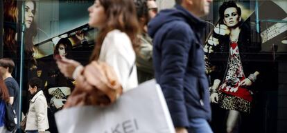 Varias personas pasan con bolsas de compras ante una de las tiendas de la c&eacute;ntrica calle Preciados de Madrid.