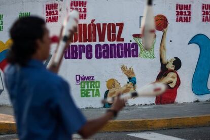 La campaña se lanzó hace un mes en la zona de Valles del Tuy, aledaña a Caracas, y se ha difundido a través de murales en las calles, banderas, pendones, camisetas o gorras. En la imagen un hombre hace malabares frente a un mural con un grafiti de Hugo Chávez, en el que el presidente aparece como un jugador de baloncesto, el martes 21 de agosto en el centro de Caracas.