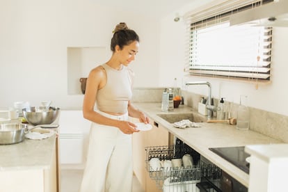 A young woman enjoys the pleasure of loading the dishwasher.