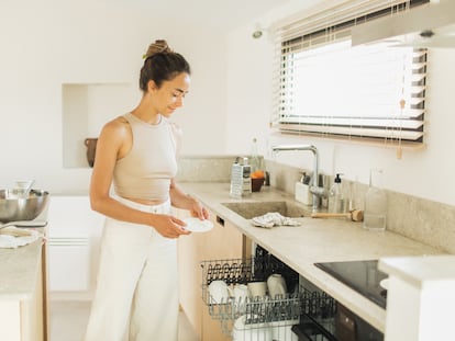 A young woman enjoys the pleasure of loading the dishwasher.