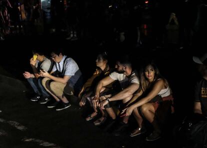 Varios jóvenes, sentados en la acera frente al hotel Row NYC, a la espera del retorno de la corriente eléctrica.