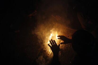 Un migrante se calienta las manos en un fuego dentro de un almacén utilizado como refugio, en Belgrado (Serbia).
