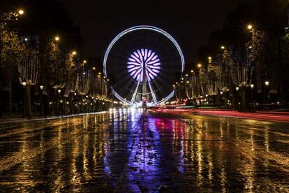 Luces de navidad cuelgan de árboles durante la noche en la avenida de los Campos Elíseos, en París (Francia).

