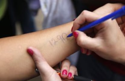 Ciudadanos de San Cristóbal escriben un número en sus brazos para marcar su turno en la cola del supermercado.