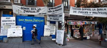 08.00. Entrada de la caseta azul donde vive acampado el matrimonio jubilado con su hijo de 42 años en coma. Todavía duermen. El espacio interior tiene menos de 30 metros cuadrados. Es habitación, sala y cocina. Llevan un año y cinco meses allí. Al fondo se ve la fachada de una sede del Ministerio de Justicia.