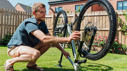 Un chico poniendo a punto su bicicleta en el jardín de su casa.