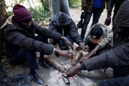 Migrantes sudaneses calientan sus manos al fuego en un bosque de Ouistreham donde pasan las noches, cerca de Caen (Francia).