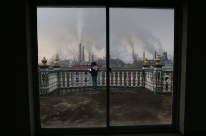 Una niña lee un libro en el balcón de su casa mientras se eleva el humo de las chimeneas de una planta de acero en la ciudad de Quzhou (China).