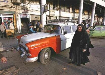 Una mujer iraquí pasa junto a un viejo Chevrolet, utilizado como taxi en la ciudad de Mosul.