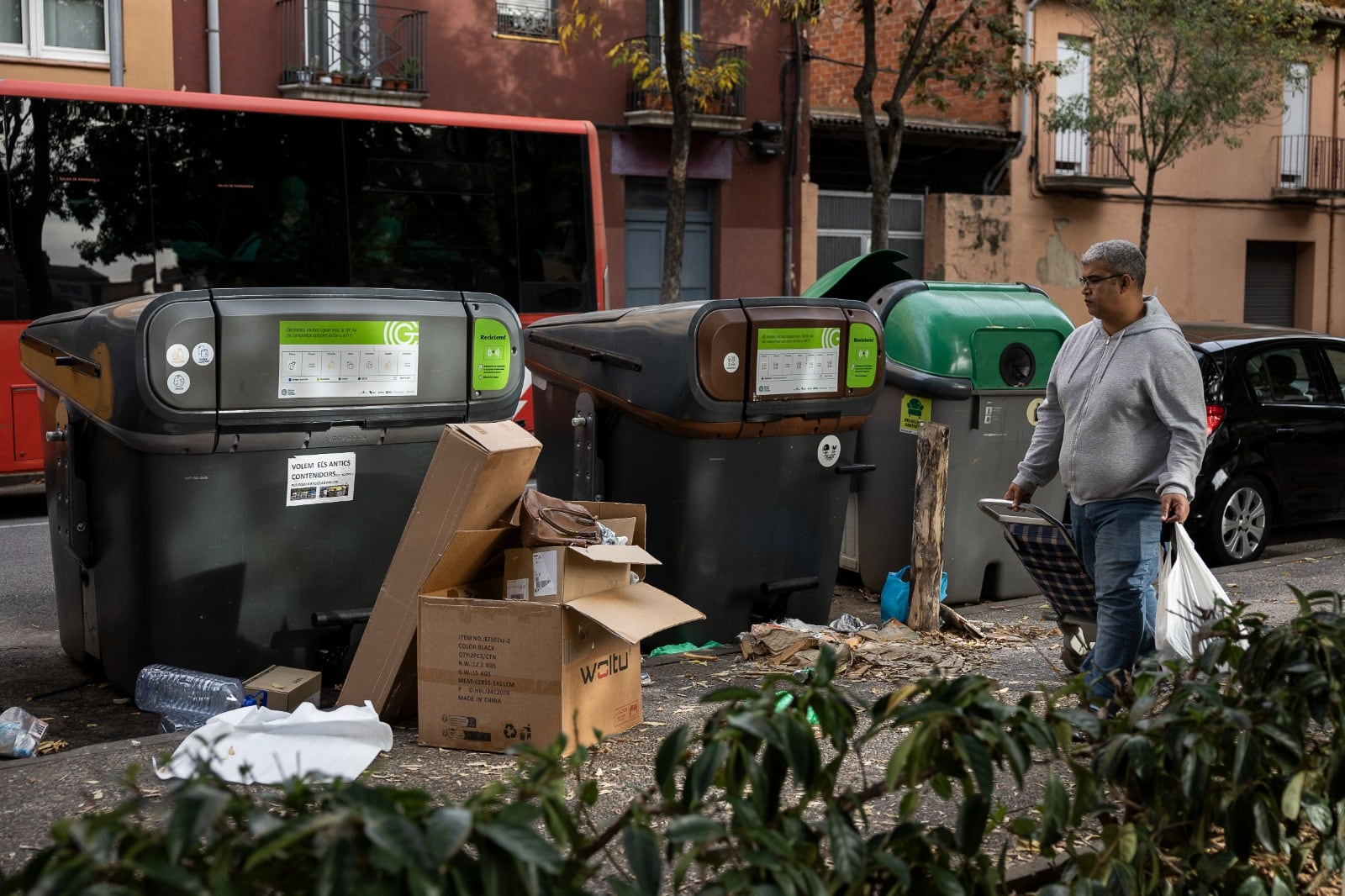 Un vecino se dispone a arrojar la basura en unos contenedores rodeados de cajas de cartón.