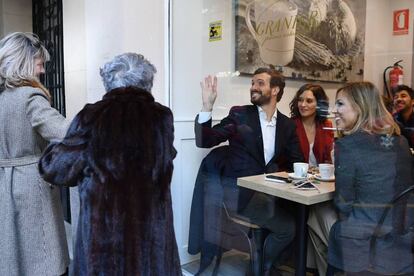 El candidato del PP a las generales, Pablo Casado, sentado junto a la presidenta de la Comunidad de Madrid, Isabel Díaz Ayuso, y su esposa, Isabel Torres, saluda a dos mujeres desde la cafetería donde han desayunado tras votar.